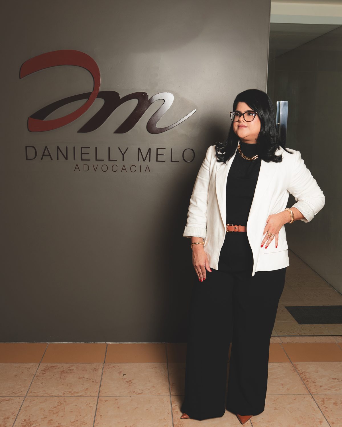 Dra. Danielly Melo diante do logotipo do escritório, em João Pessoa