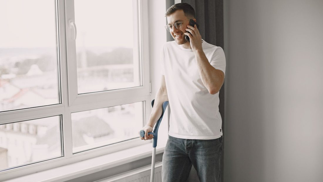 Homem com muleta falando ao telefone em casa