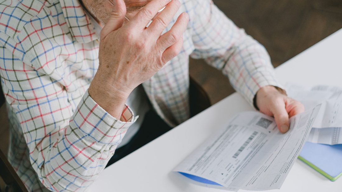 Senhor com a mão na cabeça olhando as contas e cartas sobre a mesa